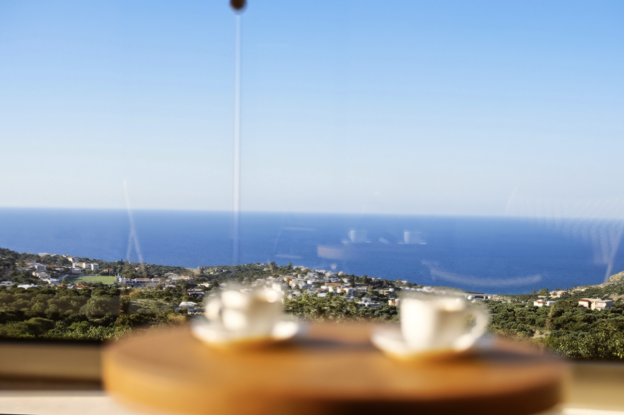 Blick durchs Fenster mit Kaffeetassen im Vordergrund auf Gerani und das Meer